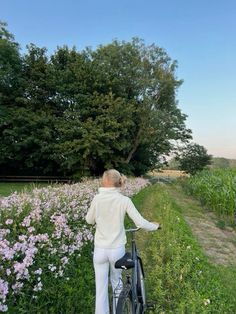 a woman standing next to a bike on a lush green field filled with purple flowers