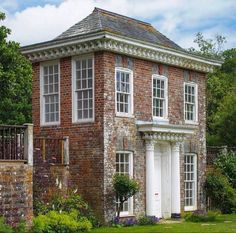 an old brick house with white doors and windows on the front lawn, surrounded by greenery