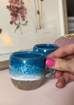 two blue mugs sitting on top of a table next to a framed flower painting