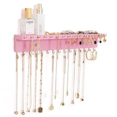 a pink jewelry rack with lots of necklaces hanging from it's sides and two bottles on the other side