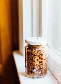 a jar filled with granola sitting on top of a window sill next to a window