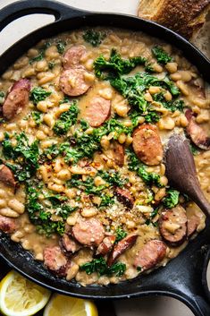 a skillet filled with beans, sausage and kale on top of a table