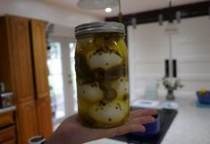 a hand holding a jar filled with pickles in a kitchen area next to a counter