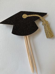 black and gold graduation hat on top of two wooden sticks with glitter decorations around it