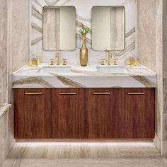 a bathroom with marble counter tops and two sinks in the center, gold faucets on either side