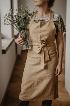 a woman wearing an apron holding flowers in her hand