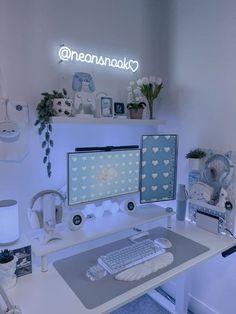 a white desk with two computer monitors and a keyboard on it, in front of a neon sign