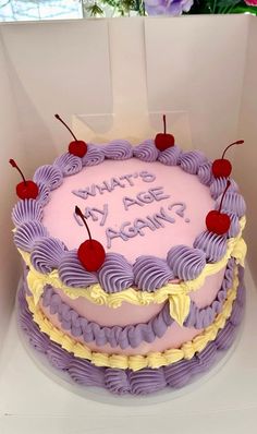 a birthday cake with purple frosting and cherries on top in a white box