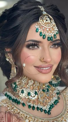 a woman wearing a green and gold bridal outfit with jewelry on her head, nose ring