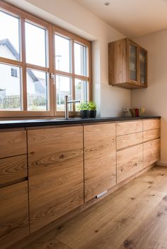 a kitchen with wooden cabinets and black counter tops in front of large windows, along with hardwood flooring