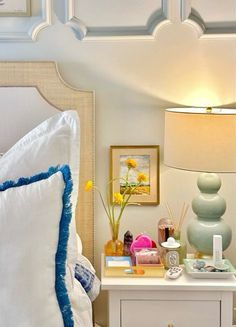 a white bed topped with pillows and a night stand next to a nightstand filled with items