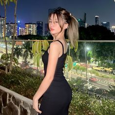 a woman in a black dress is standing on a balcony overlooking the city at night