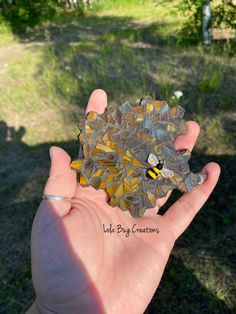 a hand holding up a small piece of broken glass in the shape of a bee