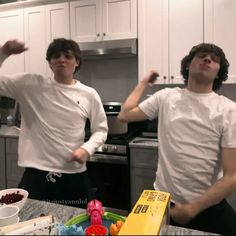 two young men standing next to each other in a kitchen