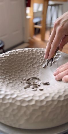 a person is cutting something out of a large white bowl with scissors on top of it