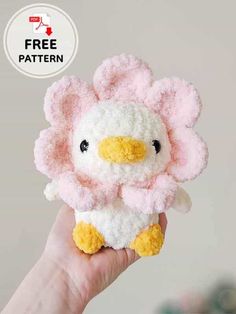 a hand holding a pink and white stuffed animal with a yellow beak on it's face