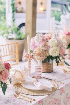 the table is set with pink and white flowers in vases, gold place settings, and napkins