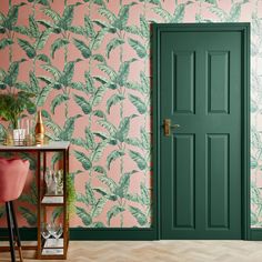 a green door in front of a pink wallpapered room with a plant on the floor