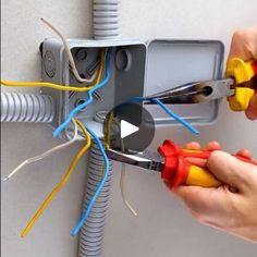 two hands are holding pliers and wires in front of an electrical box that is connected to the wall