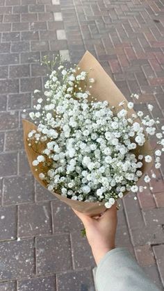 a person holding a bouquet of white flowers on a brick walkway in front of a building