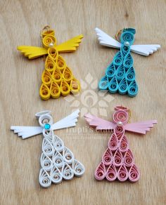 four different colored paper angel ornament on a wooden table with scissors and thread