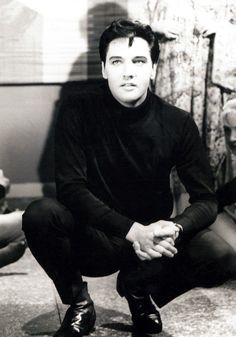 a black and white photo of a man sitting on the floor with his hands together