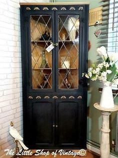 a black china cabinet with glass doors and flowers in vases on the floor next to it