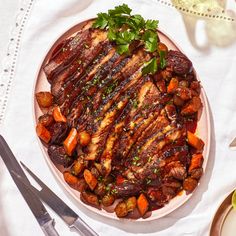 a white plate topped with meat and veggies on top of a table next to utensils