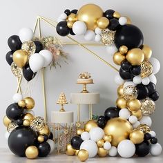 black, white and gold balloons are arranged in the shape of a wreath on a table