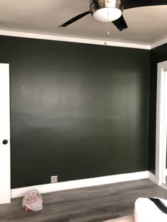 an empty room with dark green walls and white trim on the ceiling, while a fan is hanging from the ceiling