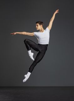 a male ballet dancer in black and white is doing a split leap on the floor