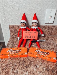 two elfs sitting on top of a counter next to orange candy bar wrappers