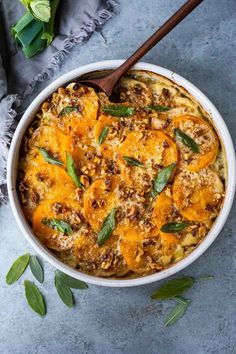 a casserole dish with squash and sage leaves in it on a gray surface