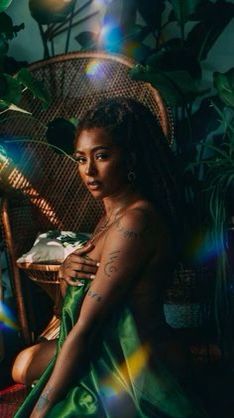 a woman with tattoos sitting on a wicker chair in front of potted plants