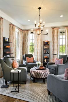 a living room filled with furniture and a chandelier hanging from the ceiling in front of two windows