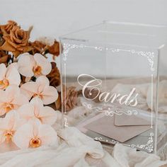 there is a clear box with some pink flowers in it and an envelope next to it