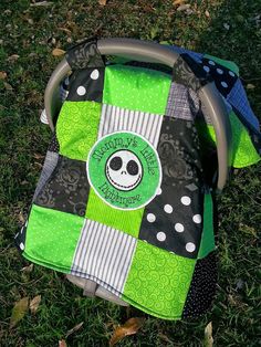 a green and black patchwork diaper bag with a skull on it sitting in the grass