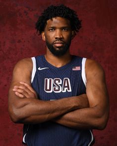 a basketball player with his arms crossed posing for a photo in front of a red background