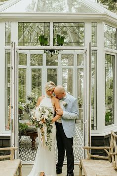 a bride and groom standing in front of a white greenhouse with lots of glass doors