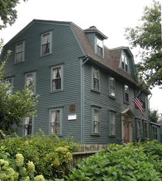 a large gray house sitting in the middle of a lush green field