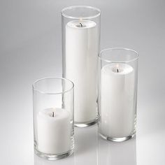 three white candles sitting next to each other in glass vases on a reflective surface