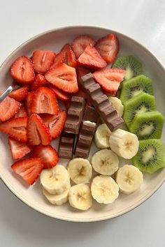 a white plate topped with sliced strawberries and kiwis next to chocolate bars