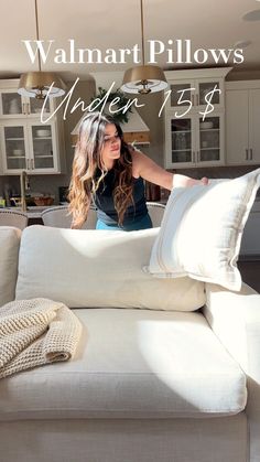 a woman sitting on top of a white couch in a living room next to pillows