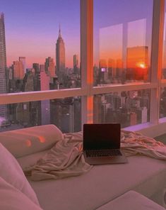 an open laptop computer sitting on top of a bed in front of a large window