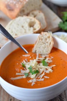 a bowl of tomato soup with parmesan cheese and bread on the side, ready to be eaten