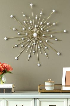 a white table topped with a vase filled with flowers next to a wall mounted sunburst