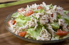 a salad with chicken and tomatoes in a glass bowl on top of a wooden table