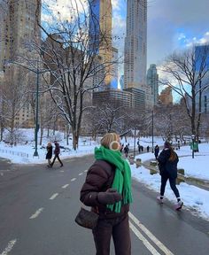 a woman standing on the side of a road in front of tall buildings and snow covered ground