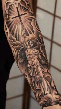 a man's arm with an angel holding a cross and clouds in the background