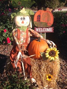 a scarecrow sitting on top of a hay bale next to a welcome sign